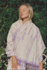 Woman wearing a purple tie-dye yoga towel with purple accents against a green leafy background